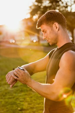 Park halindeki kol saatine mercekle bakan genç çekici bir adamın portresi.