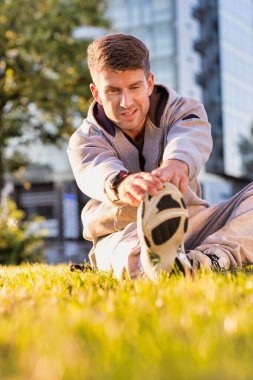Genç çekici bir adam parkta bacaklarını açıyor.