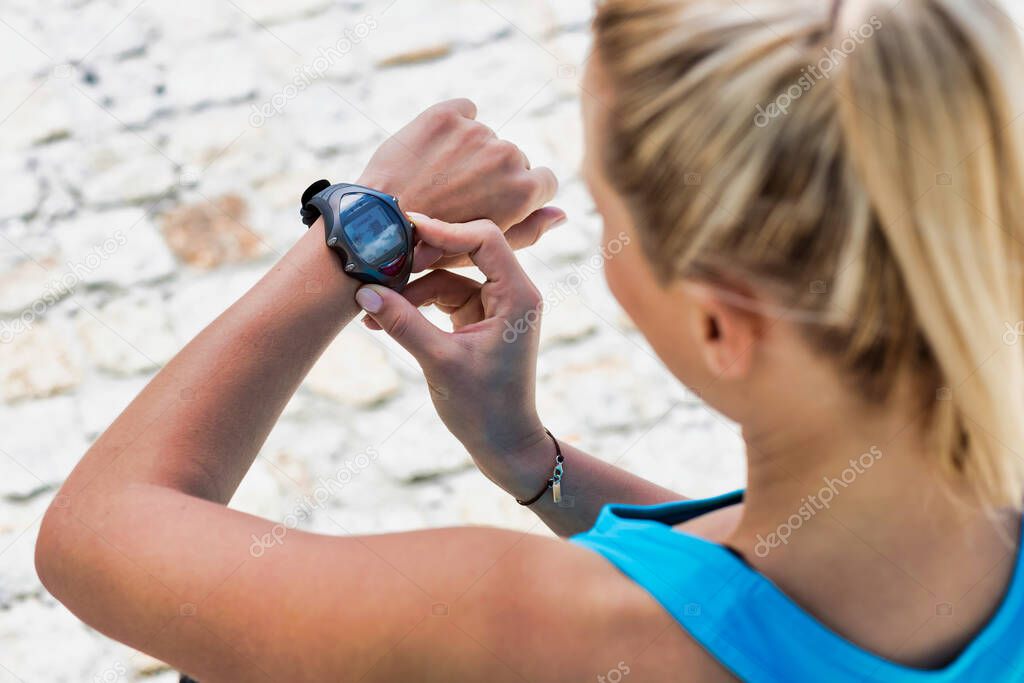 High angle view of young attractive woman looking at her wristwartch after running in park
