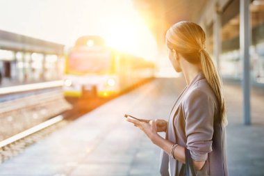 Tren istasyonunda beklerken akıllı telefon kullanan bir iş kadını portresi.