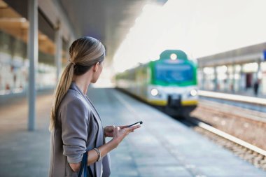 Tren istasyonunda beklerken akıllı telefon kullanan bir iş kadını portresi.