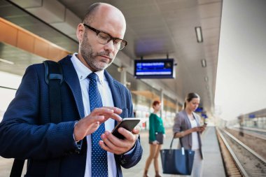 Tren istasyonunda beklerken akıllı telefon kullanan işadamının portresi