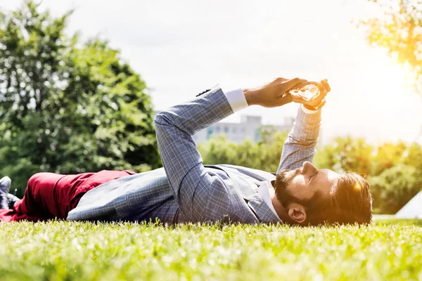 Genç Çekici Adamı Çimlerin Üzerinde Yatarken Dijital Tablet Kullanıyor — Stok fotoğraf