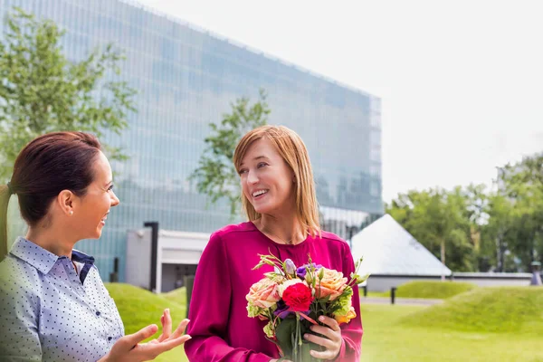 花の花束を持ちながら友人と話しているビジネスマンの女性 — ストック写真