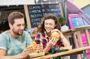 Genç ve çekici bir çift yemek kamyonuna karşı hamburger yiyor.