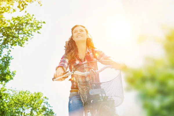 都会の真ん中でレンズフレアを背景に自転車に乗りながら微笑む若い美女の肖像画 — ストック写真
