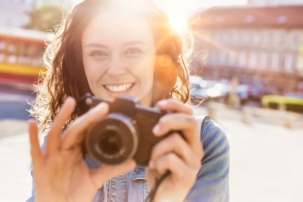 Young attractive woman holding camera and taking photo with lens flare in background