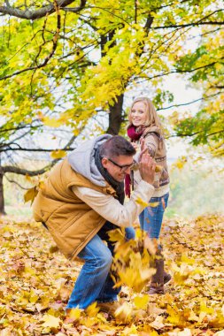 Parkta akçaağaç yapraklarıyla oynayan olgun bir çiftin portresi