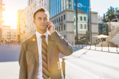 Kaldırımda yürürken gülümseyen ve telefonla konuşan olgun, kendinden emin iş adamının portresi.