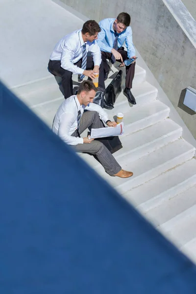 休憩時間にビジネスプランを準備しながら階段に座るハンサムなビジネスマンのグループ — ストック写真