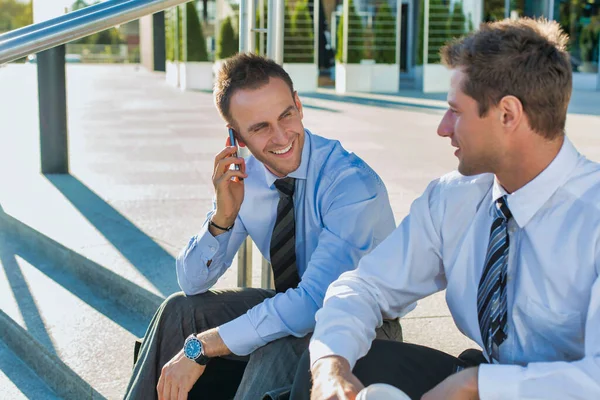 成熟したビジネスマンは笑顔で 同僚と座っている間にスマートフォンで話しています — ストック写真
