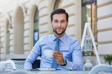Kafede oturup kahve içen genç ve çekici iş adamının portresi.
