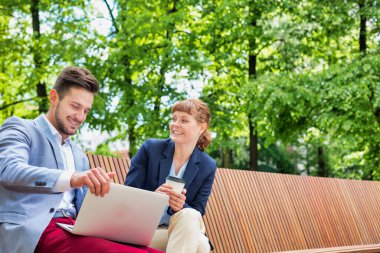 İşadamı bankta otururken güzel bir iş kadınıyla dizüstü bilgisayarda planları tartışıyor.