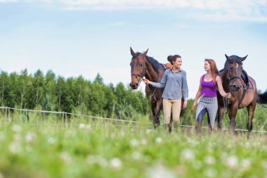 Çiftlikte atlarıyla konuşurken gezen öğretmen ve öğrenci portresi.