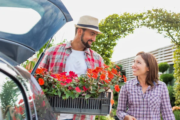 在花园商店里与女人交谈时 成熟园丁把花放在汽车行李箱上的画像 — 图库照片