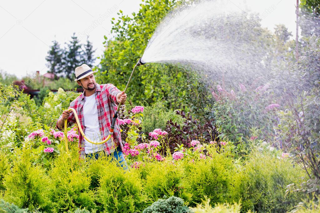 Photo of male gardener watering plants in garden shop