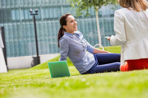 草の上に座っている間 ビジネスマンの女性は笑顔で同僚と話しています — ストック写真
