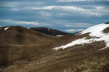 Kar henüz dağlarda tamamen erimedi, bulutlar gökyüzünde yüzüyor ve dağlarda gölgeler oluşturuyor.