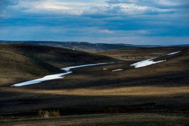 Kar henüz dağlarda tamamen erimedi, bulutlar gökyüzünde yüzüyor ve dağlarda gölgeler oluşturuyor.