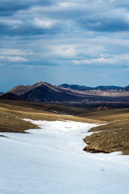 Kar henüz dağlarda tamamen erimedi, bulutlar gökyüzünde yüzüyor ve dağlarda gölgeler oluşturuyor.