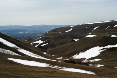 Kar henüz dağlarda tamamen erimedi, bulutlar gökyüzünde yüzüyor ve dağlarda gölgeler oluşturuyor.