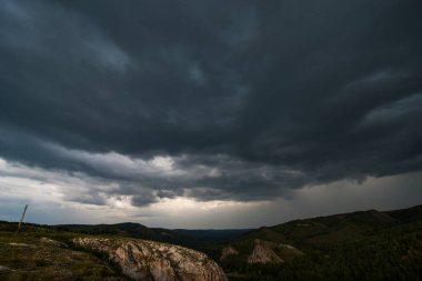 Batan güneşle aydınlanan küçük dağlar ve gökteki fırtına bulutları.