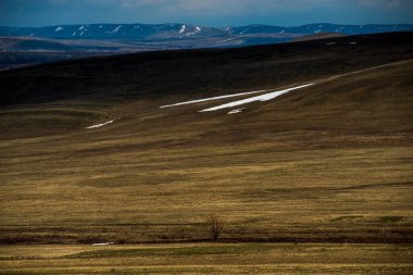 Bulutlar gökyüzünde süzülür, dağlarda bir ışık gölgesi deseni oluşturur.