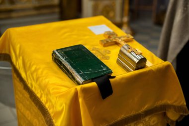Eski bir kilise kitabı ve haç sarı bir masa örtüsünün üzerinde yatıyor.