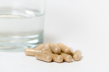 Tıbbın kapsülleri bir bardak suyun arka planında yakın plan, sığ alan derinliği.