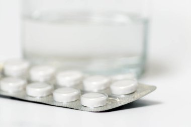 İlaç hapları bir bardak suyun arka planında yakın plan, sığ alan derinliği.