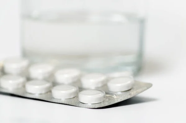 İlaç hapları bir bardak suyun arka planında yakın plan, sığ alan derinliği.