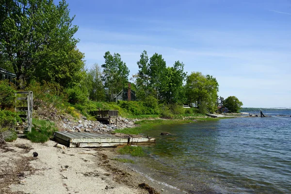 Rocky kystlinje med brygge i avstand og grønne trær – stockfoto