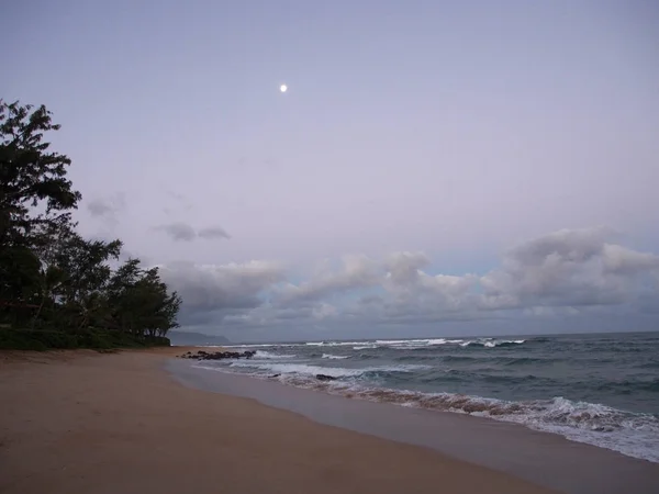 Las olas rodan en la orilla al amanecer con la luna en el cielo —  Fotos de Stock