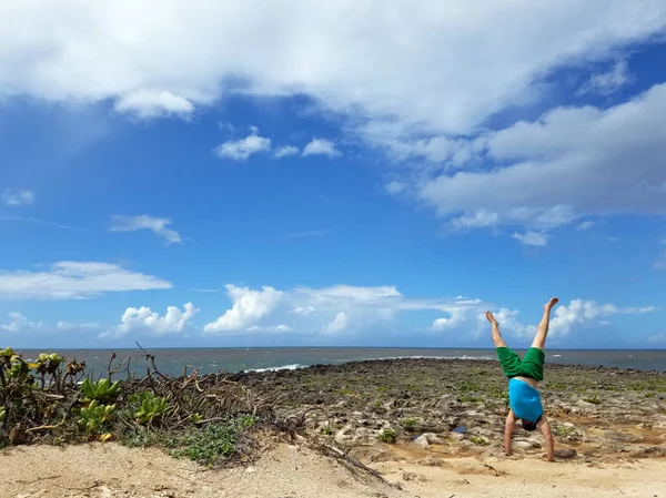 Mand Håndstående på stranden som bølge nedbrud og skyer i himlen - Stock-foto