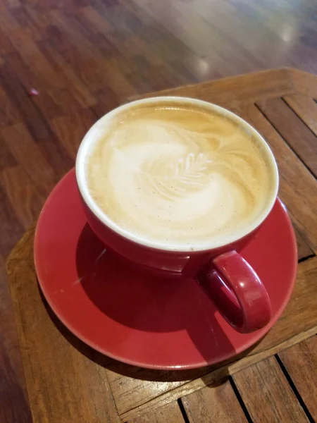 Red cup of Cappuccino on saucer with a leaf pattern in foam — Stock Photo, Image