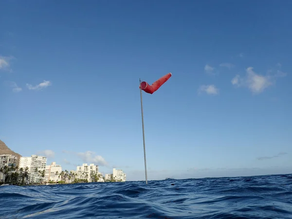 Flag pole with wind sock rises above the wavy waters of Waikiki — Stock Photo, Image