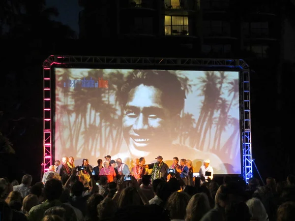 Duke Kahanamoku imagen en la pantalla con la gente en el escenario después de soltar — Foto de Stock