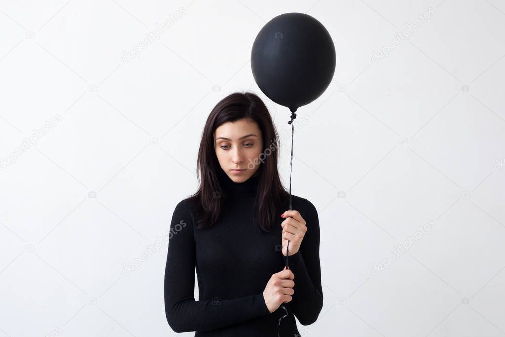 A sad girl holds a black balloon in her hands. 