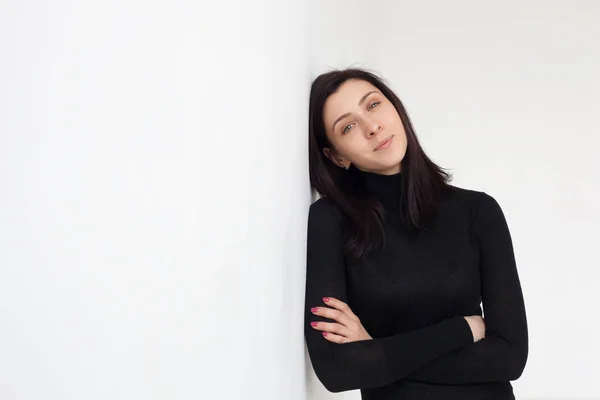 Una chica vestida de negro está parada junto a la pared blanca . — Foto de Stock