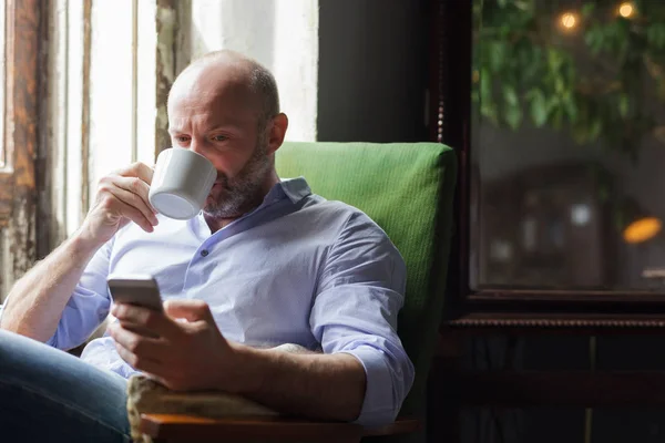 Мужчина пьет кофе и проверяет новости по телефону. — стоковое фото