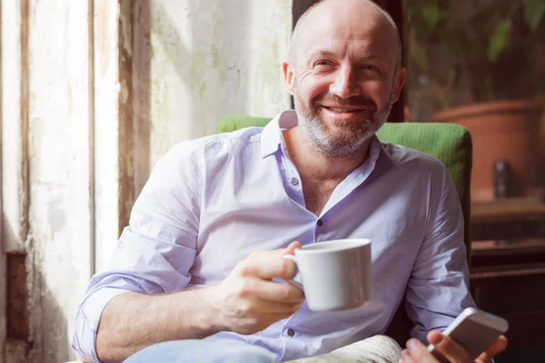 A man drinks coffee and checks the news in the phone