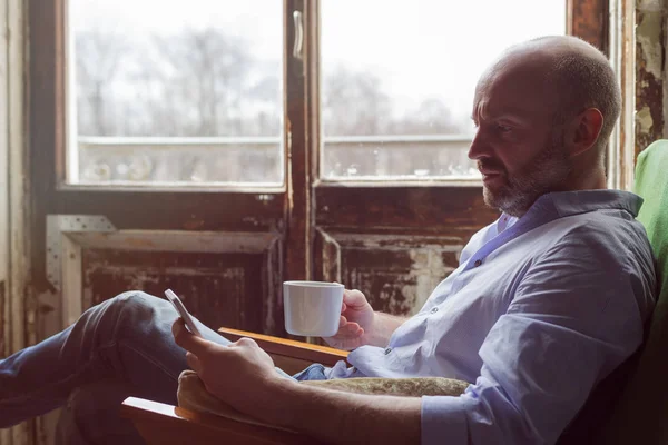 A man drinks coffee and checks the news in the phone