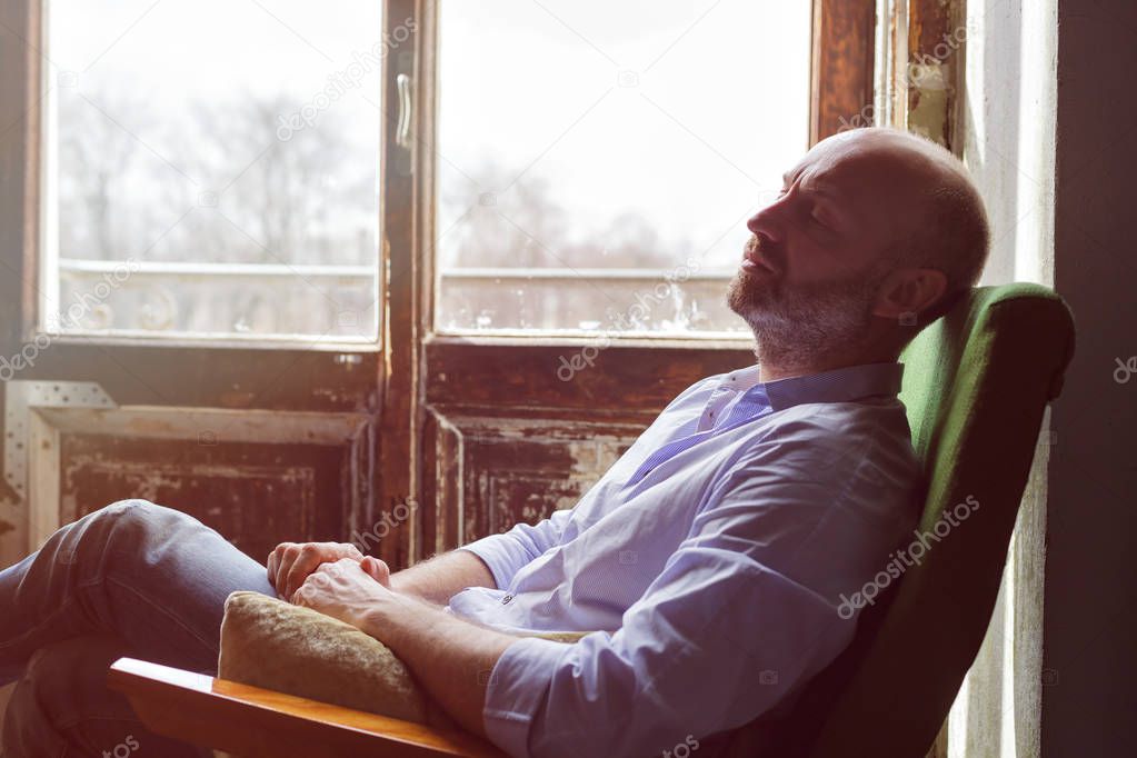 A middle-aged man is tiredly sitting in a chair. 