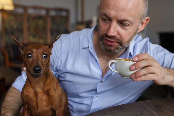 彼の犬と一緒に座っていると、お茶やコーヒーを飲む男 — ストック写真