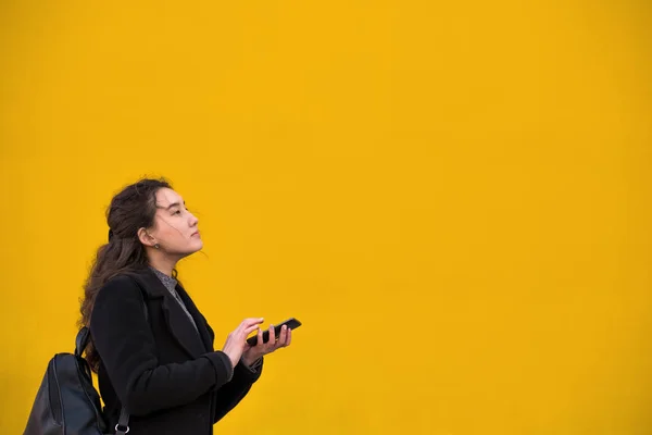 Ein asiatisches Mädchen in schwarzem Mantel und einem Handy mit der Hand geht — Stockfoto