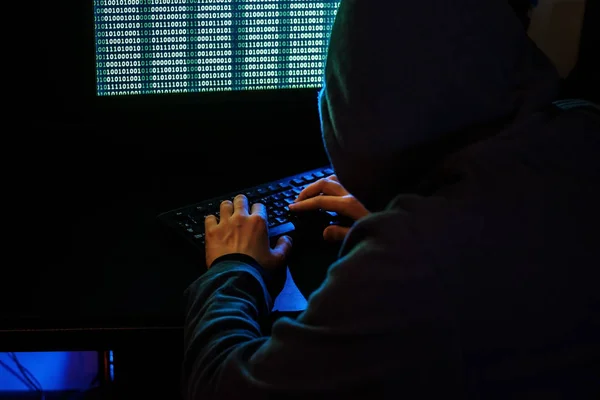 The man in the hood checks the malicious code on the keyboard. — Stock Photo, Image