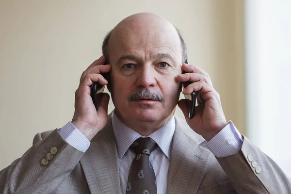 En upptagen affärsman i kostym försöker prata på två telefoner samtidigt. — Stockfoto