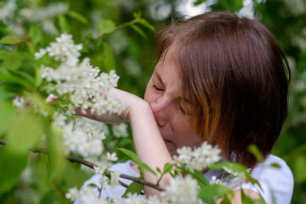 Красивая девушка стоит у цветущей птичьей вишни и чихает — стоковое фото