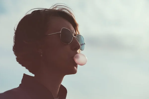Ein Mädchen mit Sonnenbrille pustet eine Kaugummiblase. — Stockfoto