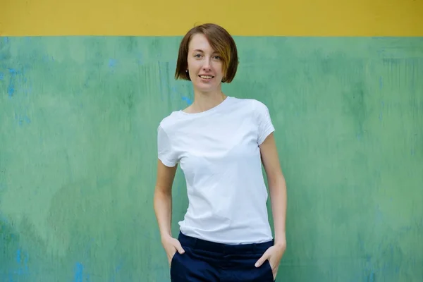 En vacker flicka med fräknar i en vit T-shirt står vid väggen — Stockfoto